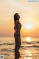 A woman standing in the ocean at sunset.