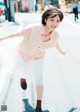 A woman in a pink shirt and white skirt is running down the street.