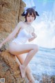 A woman in a white bathing suit sitting on a rock by the ocean.